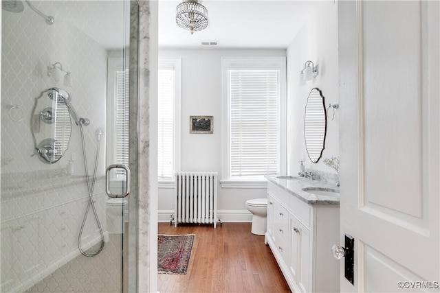 bathroom featuring hardwood / wood-style floors, radiator heating unit, vanity, a shower with shower door, and toilet