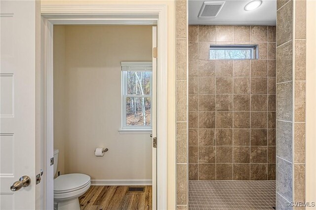 bathroom featuring tiled shower, a healthy amount of sunlight, wood-type flooring, and toilet