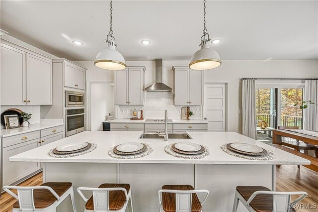 kitchen featuring wall chimney exhaust hood, hanging light fixtures, stainless steel appliances, a kitchen breakfast bar, and a kitchen island with sink