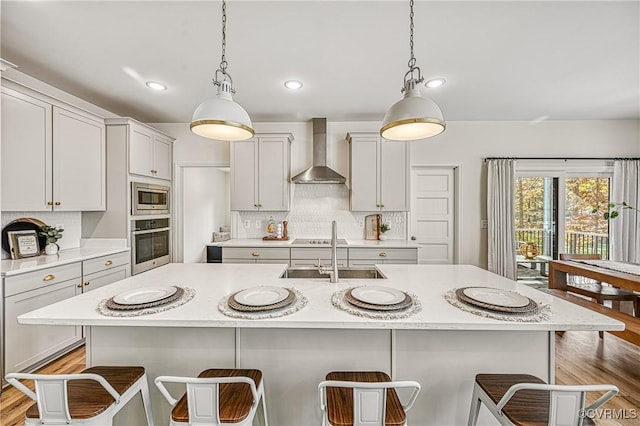 kitchen featuring a kitchen bar, a center island with sink, pendant lighting, stainless steel appliances, and wall chimney range hood