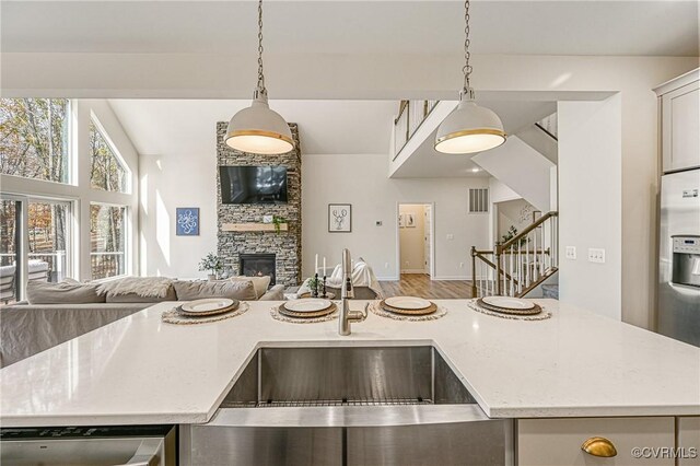 kitchen with sink, a stone fireplace, light stone counters, stainless steel fridge, and pendant lighting