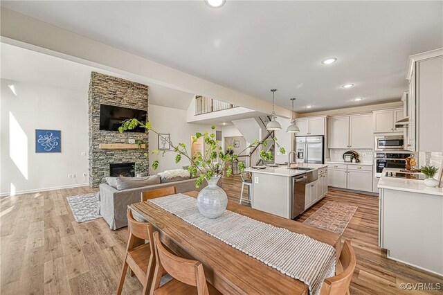 kitchen with tasteful backsplash, stainless steel appliances, pendant lighting, a center island with sink, and a stone fireplace