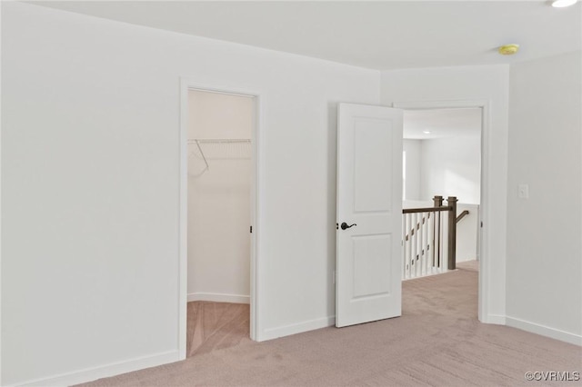 unfurnished bedroom featuring light colored carpet, a walk in closet, and a closet