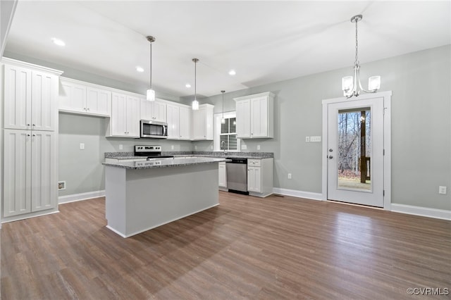 kitchen featuring stone counters, white cabinetry, hanging light fixtures, stainless steel appliances, and a kitchen island