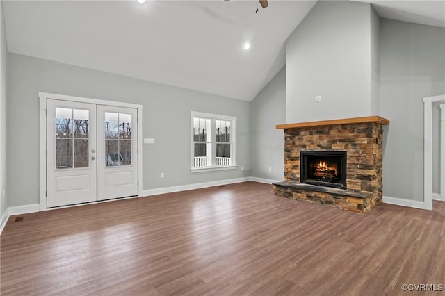 unfurnished living room featuring hardwood / wood-style flooring, ceiling fan, a stone fireplace, and french doors