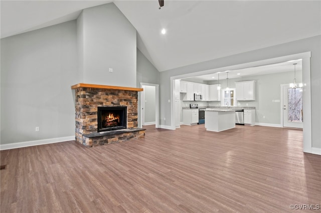 unfurnished living room with a stone fireplace, a chandelier, high vaulted ceiling, and wood-type flooring