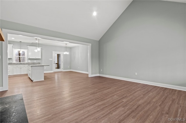 unfurnished living room with a notable chandelier, light wood-type flooring, and vaulted ceiling