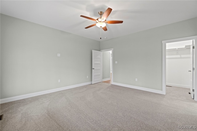 unfurnished bedroom with a closet, light colored carpet, a spacious closet, and ceiling fan