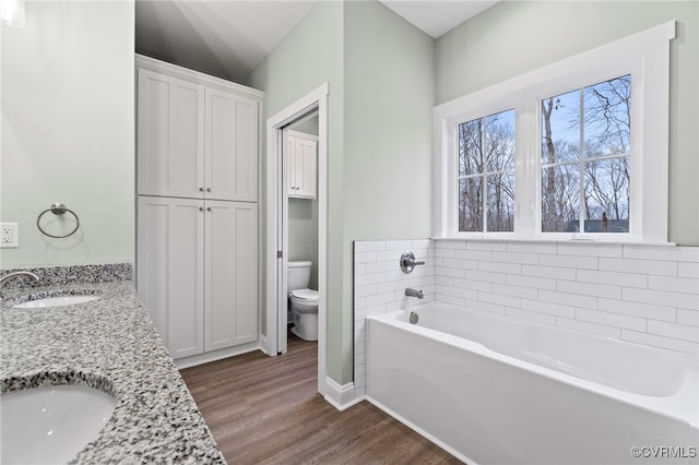 bathroom with a washtub, vanity, hardwood / wood-style flooring, and toilet