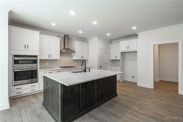 kitchen featuring a kitchen island with sink, sink, white cabinets, and wall chimney range hood