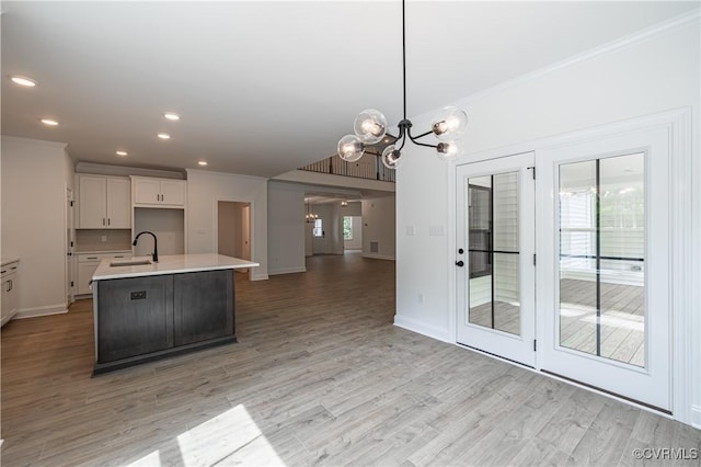 kitchen featuring sink, hanging light fixtures, a notable chandelier, an island with sink, and white cabinets