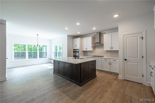 kitchen featuring white cabinetry, wall chimney exhaust hood, hanging light fixtures, stainless steel gas stovetop, and a kitchen island with sink