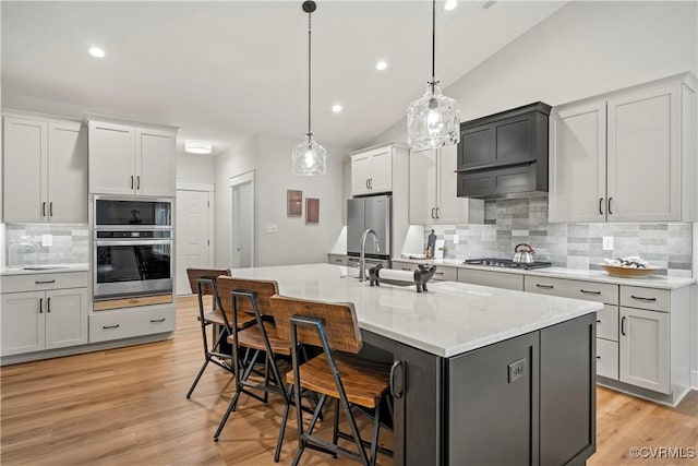 kitchen featuring tasteful backsplash, decorative light fixtures, lofted ceiling, a kitchen island with sink, and appliances with stainless steel finishes