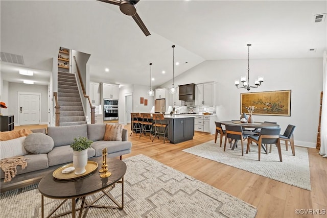 living room with lofted ceiling, light hardwood / wood-style flooring, and ceiling fan with notable chandelier