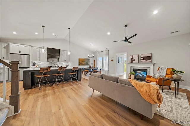 living room featuring ceiling fan, light wood-type flooring, a high end fireplace, and vaulted ceiling