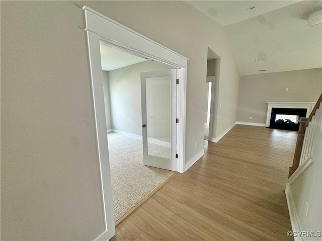 hallway featuring light wood-style floors, baseboards, and lofted ceiling