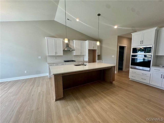 kitchen featuring stainless steel appliances, wall chimney exhaust hood, light wood-style flooring, a sink, and backsplash