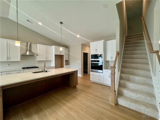kitchen featuring wall chimney exhaust hood, a sink, light wood-style floors, backsplash, and lofted ceiling
