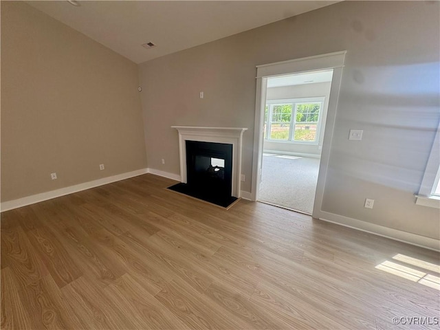 unfurnished living room with light wood-type flooring, baseboards, and a fireplace with flush hearth