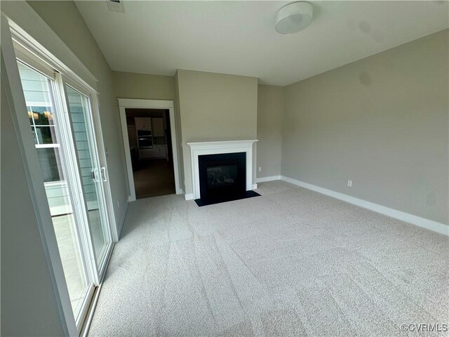 unfurnished living room featuring light colored carpet, baseboards, and a fireplace with flush hearth