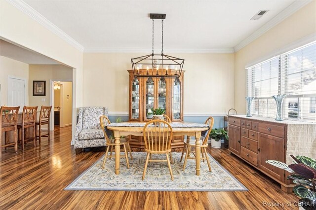 dining area with dark hardwood / wood-style flooring, ornamental molding, and an inviting chandelier