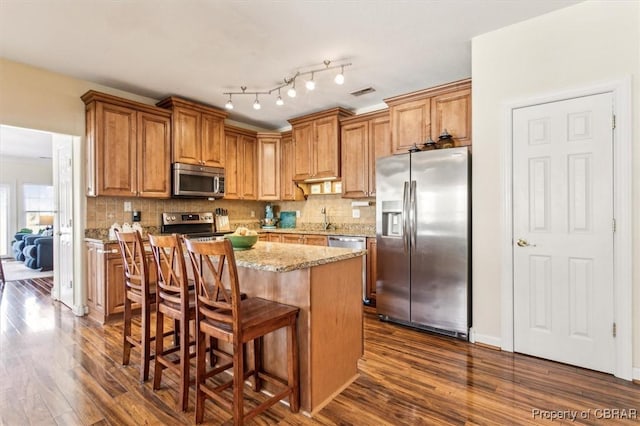 kitchen featuring a center island, dark hardwood / wood-style floors, light stone countertops, appliances with stainless steel finishes, and a kitchen bar