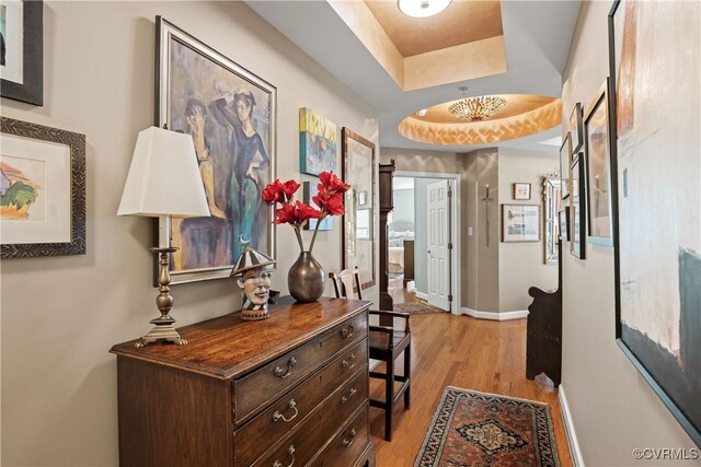 hallway with light wood-type flooring and a tray ceiling