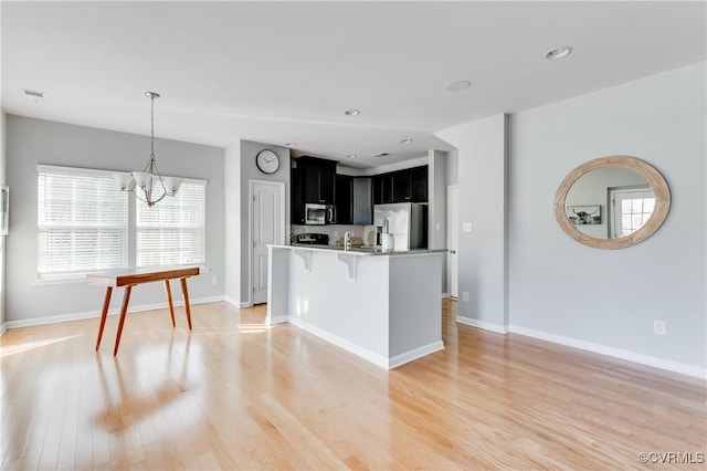 kitchen featuring stainless steel appliances, a notable chandelier, light hardwood / wood-style floors, pendant lighting, and a kitchen bar