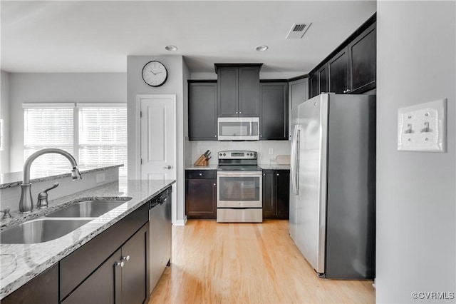 kitchen featuring decorative backsplash, light stone counters, stainless steel appliances, sink, and light hardwood / wood-style floors