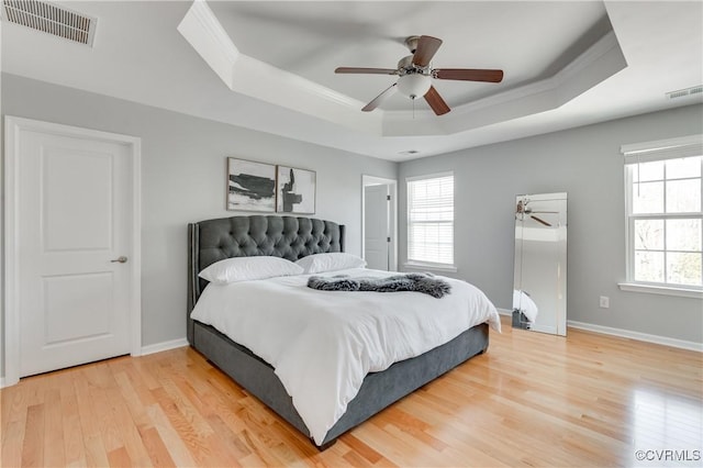 bedroom featuring ceiling fan, wood-type flooring, multiple windows, and a tray ceiling