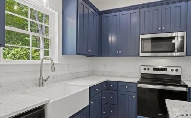 kitchen with a healthy amount of sunlight, light stone counters, sink, and appliances with stainless steel finishes