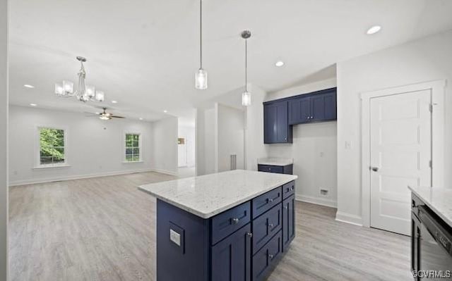 kitchen with light stone countertops, ceiling fan with notable chandelier, a kitchen island, and hanging light fixtures