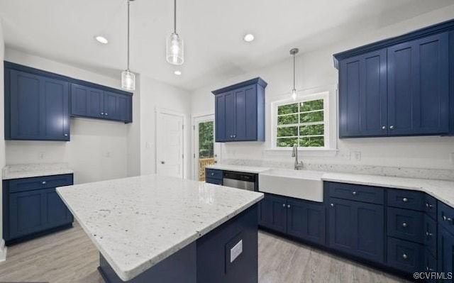 kitchen with light wood-type flooring, light stone counters, sink, a kitchen island, and hanging light fixtures