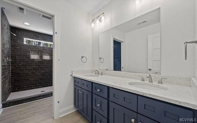 bathroom with a tile shower, vanity, and wood-type flooring