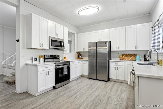 kitchen with light stone counters, stainless steel appliances, a sink, white cabinetry, and light wood finished floors