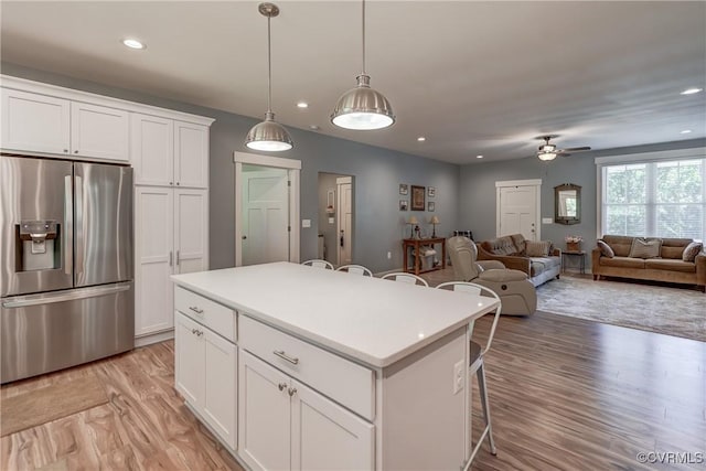 kitchen with white cabinetry, a center island, ceiling fan, a kitchen breakfast bar, and stainless steel refrigerator with ice dispenser