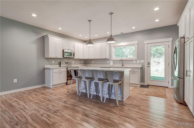 kitchen featuring light wood-type flooring, stainless steel appliances, a kitchen island, sink, and white cabinetry