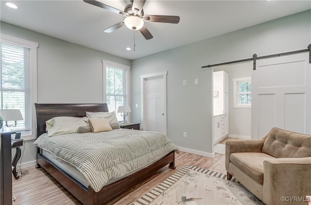 bedroom featuring ceiling fan, a barn door, and light hardwood / wood-style floors