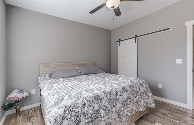 bedroom featuring hardwood / wood-style flooring, ceiling fan, and a barn door