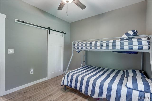 bedroom with hardwood / wood-style floors, a barn door, and ceiling fan