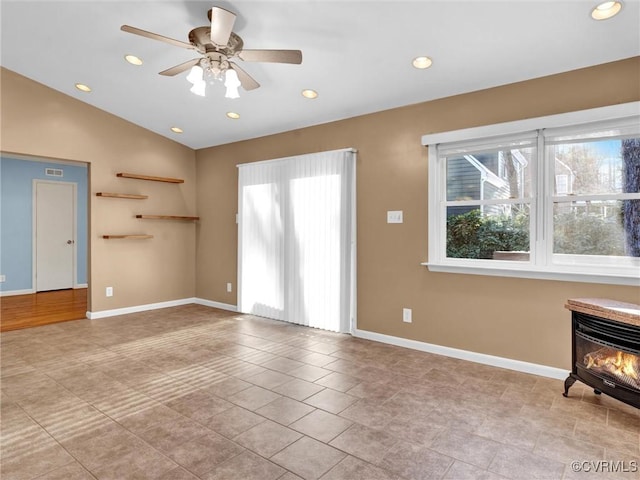 unfurnished living room with ceiling fan, lofted ceiling, a wealth of natural light, and a wood stove