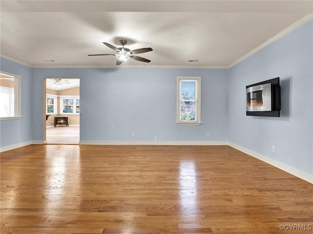 spare room with plenty of natural light, a wood stove, crown molding, and light hardwood / wood-style flooring