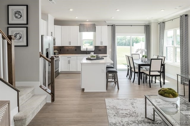 kitchen featuring a kitchen breakfast bar, tasteful backsplash, a center island, light hardwood / wood-style floors, and white cabinetry