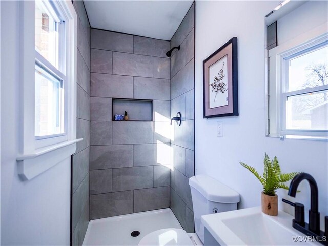 bathroom featuring sink, toilet, tiled shower, and plenty of natural light