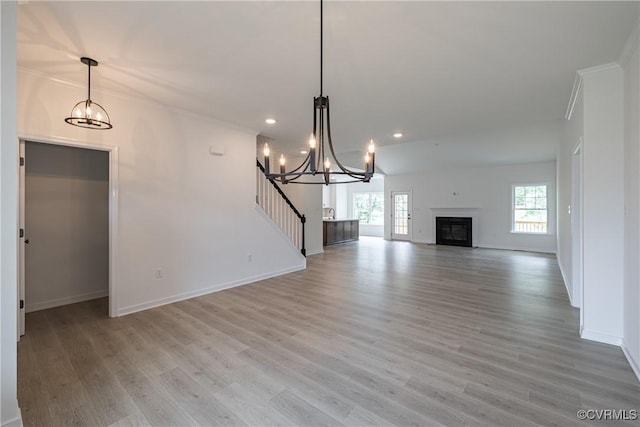 unfurnished living room with a notable chandelier, light wood-type flooring, and ornamental molding