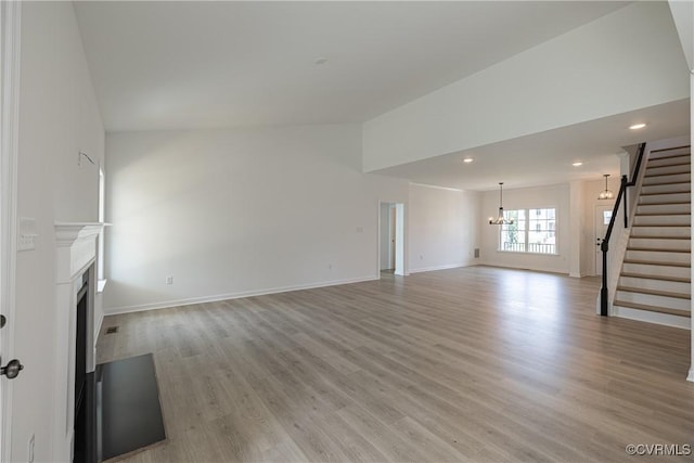 unfurnished living room featuring an inviting chandelier, lofted ceiling, and light hardwood / wood-style flooring