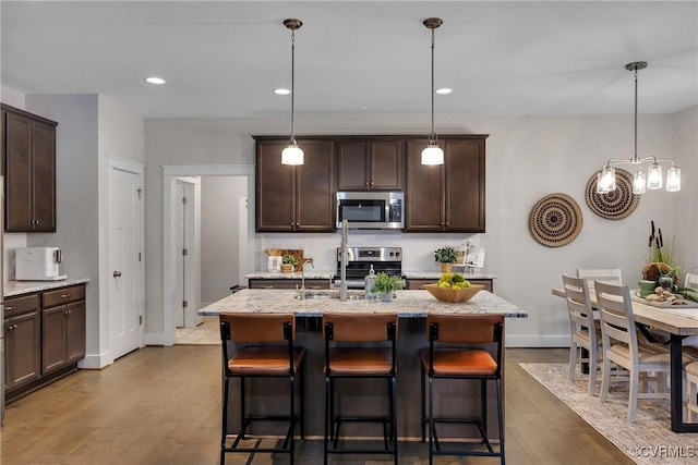 kitchen featuring hanging light fixtures, a center island with sink, hardwood / wood-style floors, and stainless steel appliances