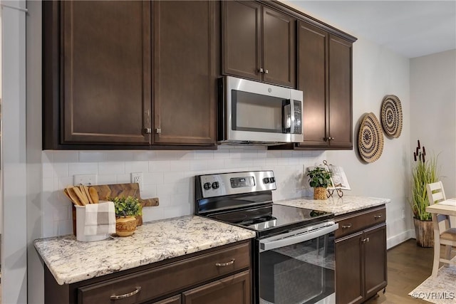 kitchen featuring decorative backsplash, appliances with stainless steel finishes, light stone counters, dark brown cabinets, and hardwood / wood-style floors