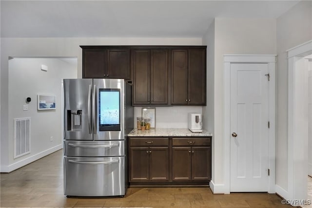 kitchen with decorative backsplash, stainless steel fridge, light stone counters, dark brown cabinets, and light hardwood / wood-style flooring