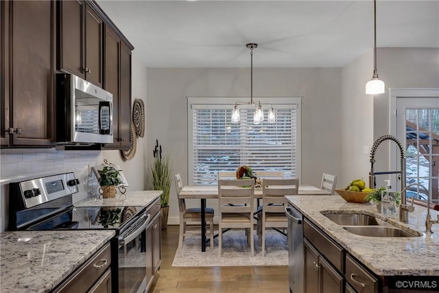 kitchen featuring dark brown cabinetry, stainless steel appliances, light stone counters, and sink